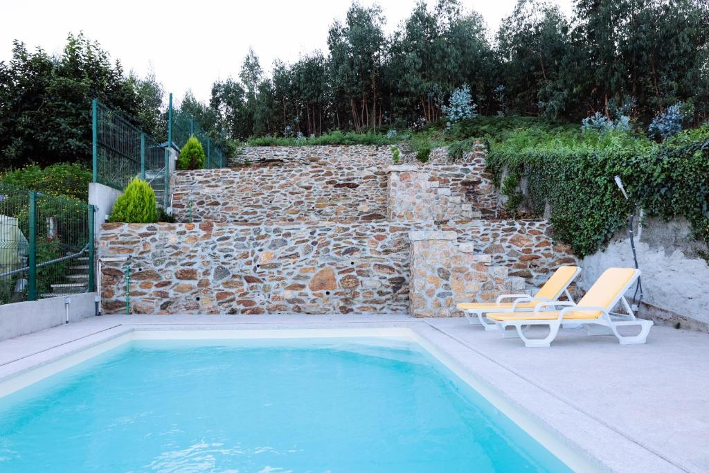 a swimming pool with two lounge chairs next to a stone wall at Casa do avô tamanqueiro in Arco de Baúlhe