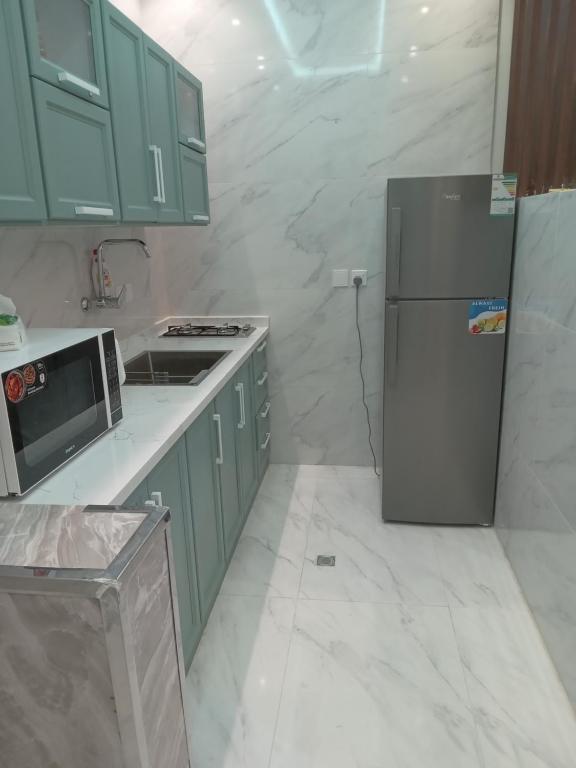 La cuisine est équipée d'armoires vertes et d'un réfrigérateur en acier inoxydable. dans l'établissement شاليه لوسيل, à Khamis Mushait