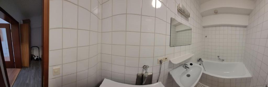 ein weiß gefliestes Bad mit einem Urinal und einem Waschbecken in der Unterkunft Ludwigsturm Appartement in Straubing in Straubing