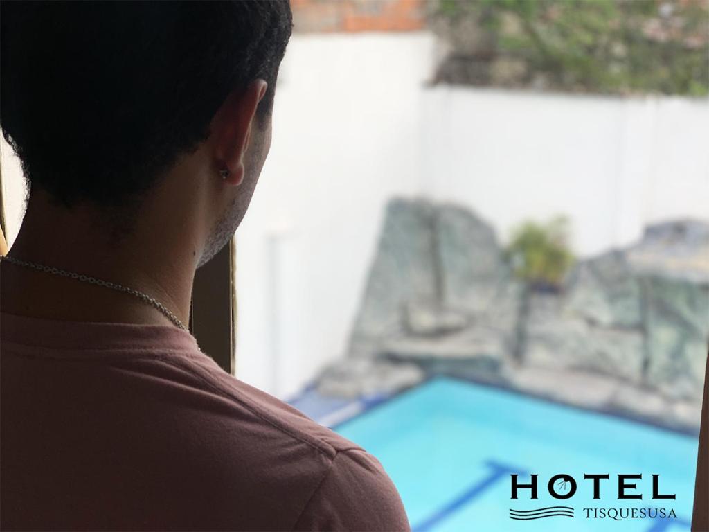 a man looking out a window at a swimming pool at El Hotel Tisquesusa in Girardot
