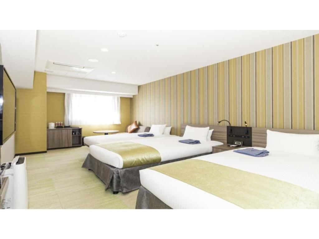 Una habitación de hotel con tres camas y una mujer sentada en la ventana. en La'gent Stay Hakodate Ekimae - Vacation STAY 88785v, en Hakodate