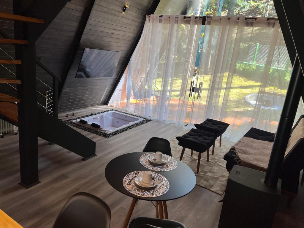 a living room with tables and chairs and a large window at Chalé Villa Nature in Campos do Jordão