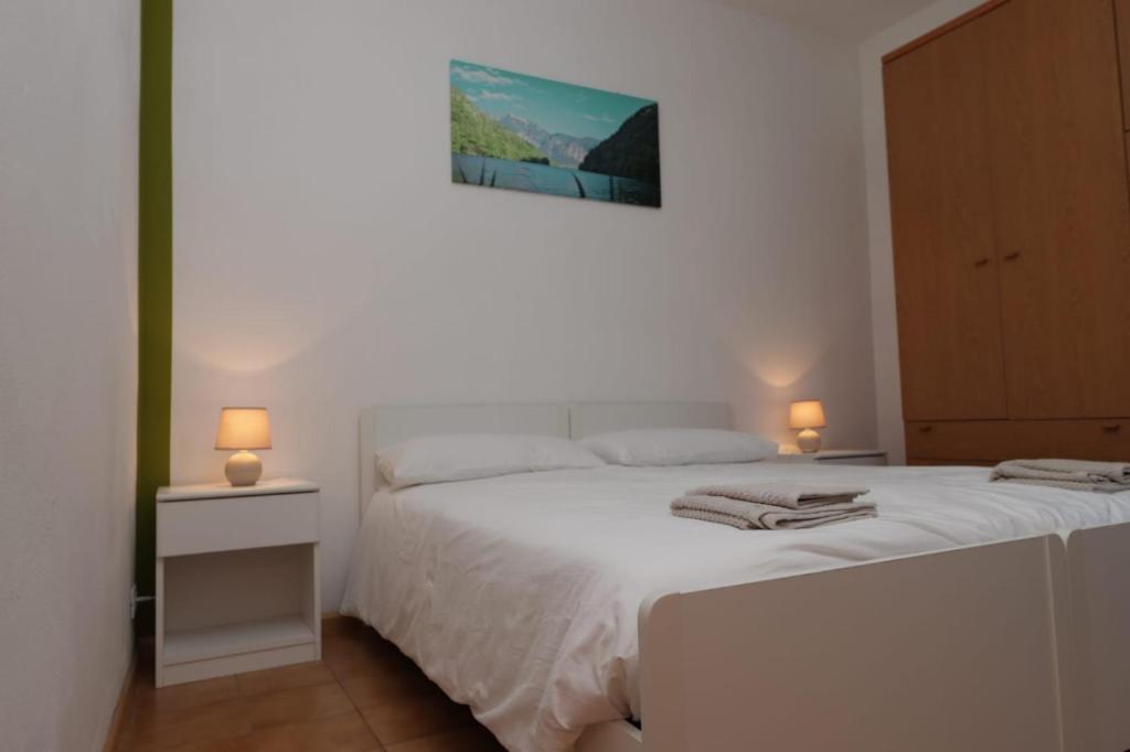 a bedroom with a white bed with two lamps on it at Appartamento Valentina in Levico Terme