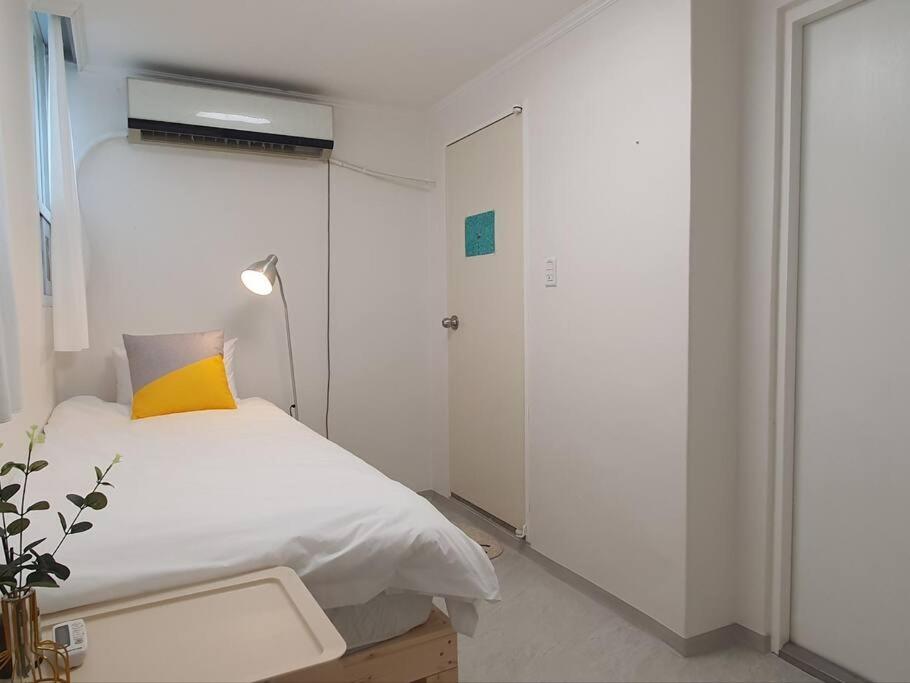 ein weißes Schlafzimmer mit einem Bett und einem gelben Kissen in der Unterkunft Coco Stay in Seoul