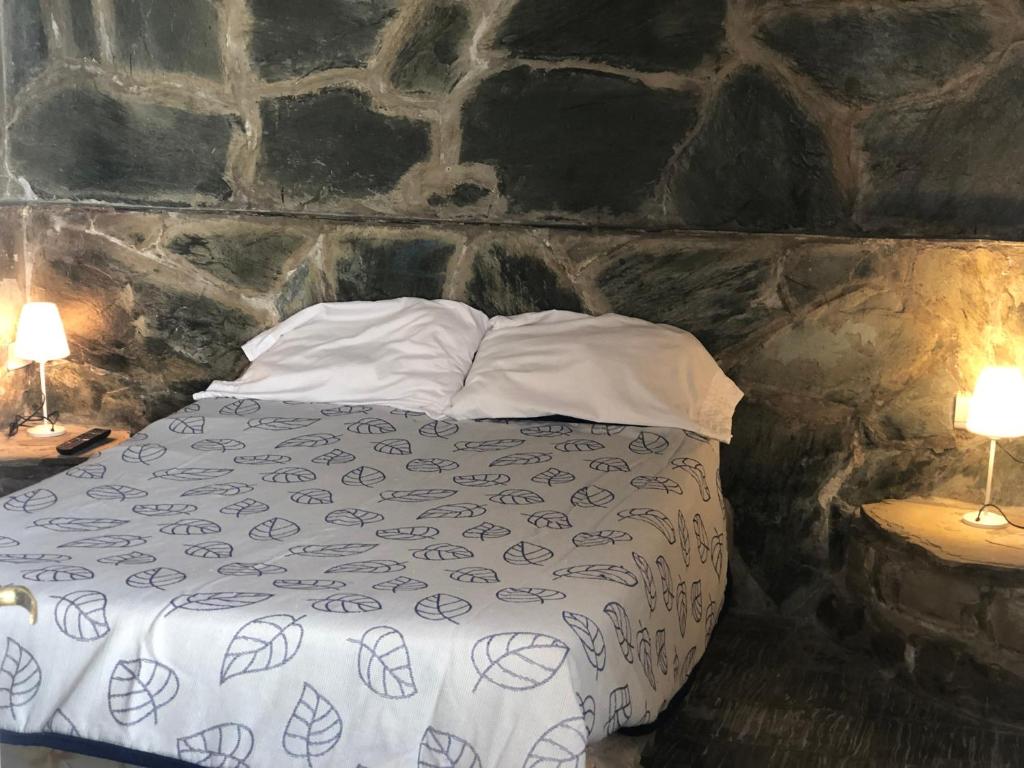 Cama en habitación de piedra con 2 lámparas en La Colonial en Salta