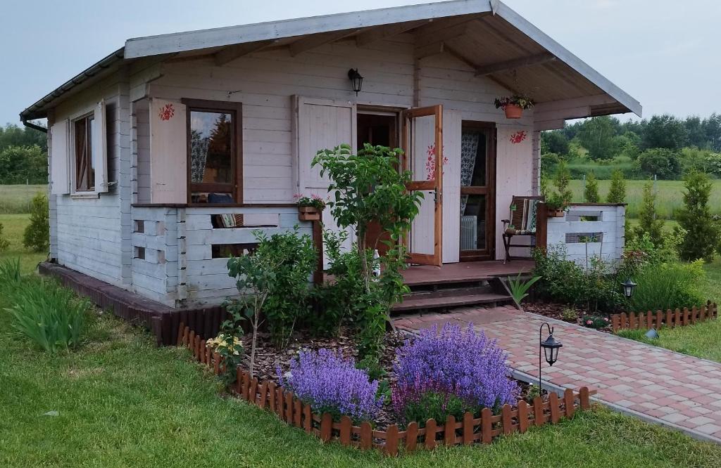 a small white house with a porch and flowers at W Malinowym Chruśniaku in Nowa Słupia