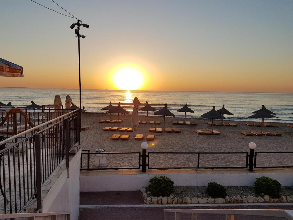 a sunset on a beach with umbrellas and the ocean at La Perla Bianca Residence in Eforie Nord