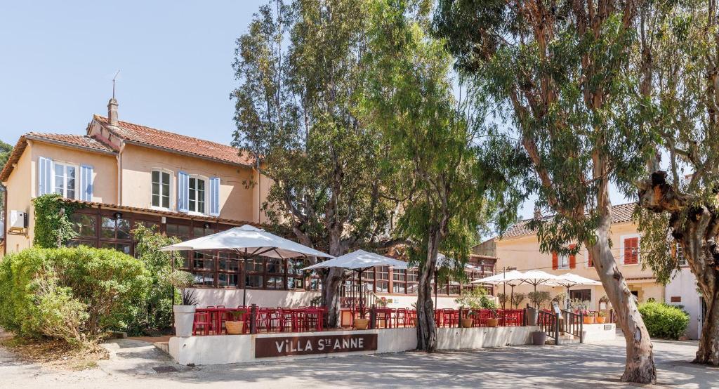 un restaurant avec des tables et des parasols en face d'un bâtiment dans l'établissement Villa Sainte Anne, à Porquerolles