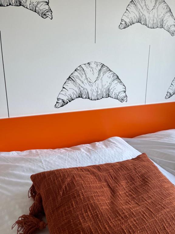 Close-up of bed corner showing croissant wallpaper, orange headboard and textured rust pillow.