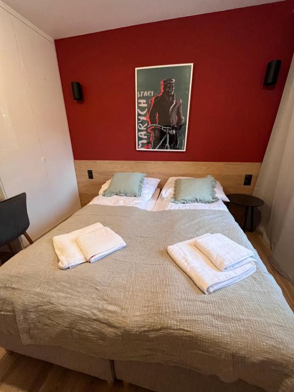 Cozy bedroom with red accent wall, double bed neatly made and folded towels on bed.