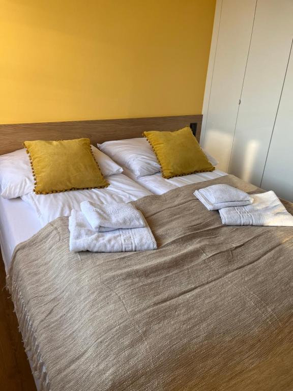 Double bed against sunny yellow wall with mustard throw pillows and neatly folded towels.