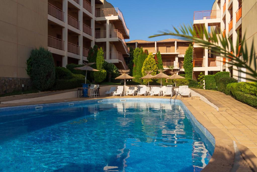 a swimming pool with chairs and umbrellas next to a building at Частен апартамент в затворен комплекс in Sinemorets