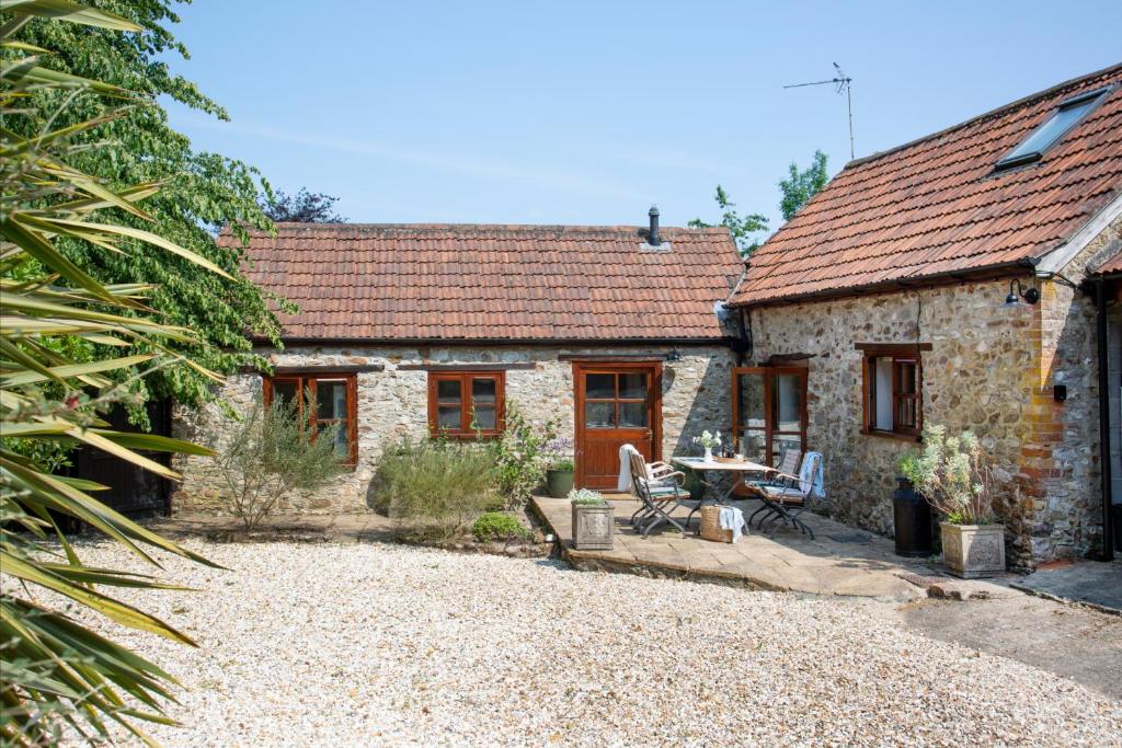 een stenen huisje met een tafel en stoelen ervoor bij Whitley Farm Dairy in Northleigh