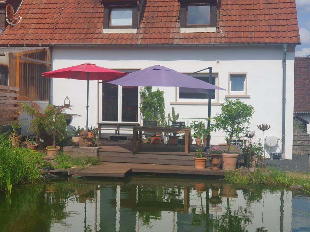 ein Haus mit zwei Sonnenschirmen auf einer Terrasse neben einem Teich in der Unterkunft Ferienwohnung Katrin in Mettlach