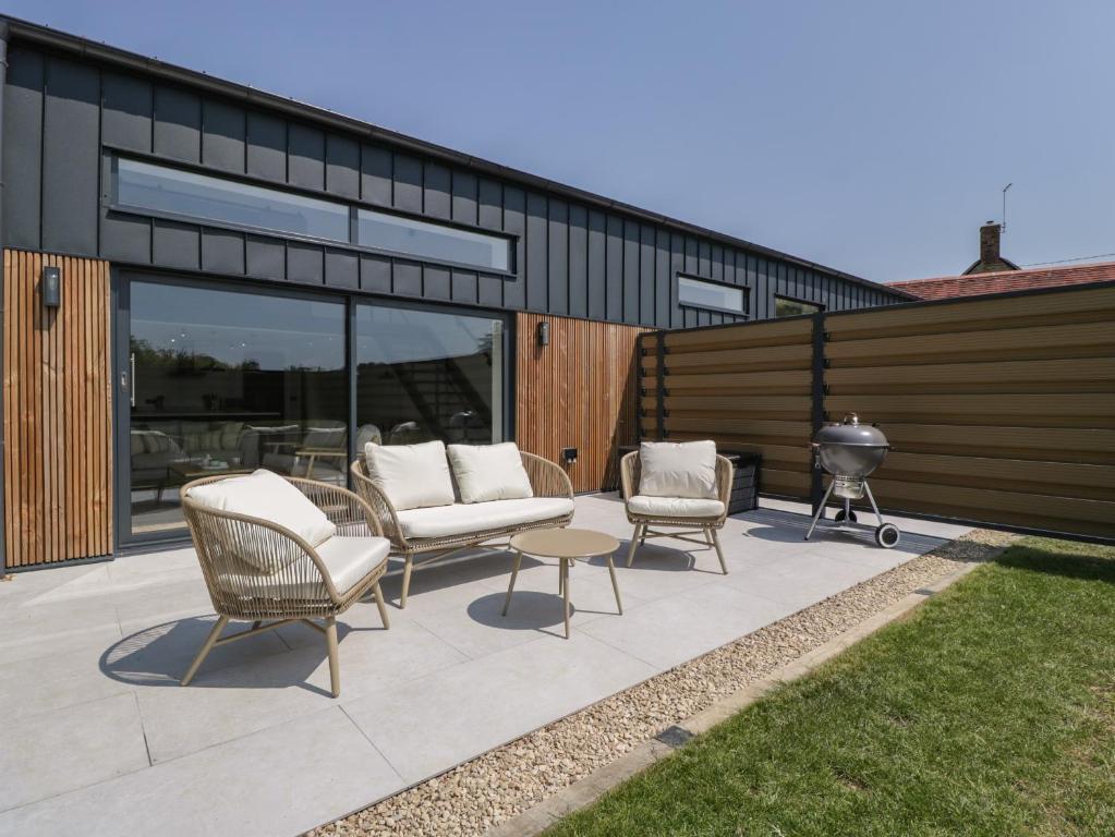 a patio with three chairs and a fire grill at Tilia Barn in Wincanton