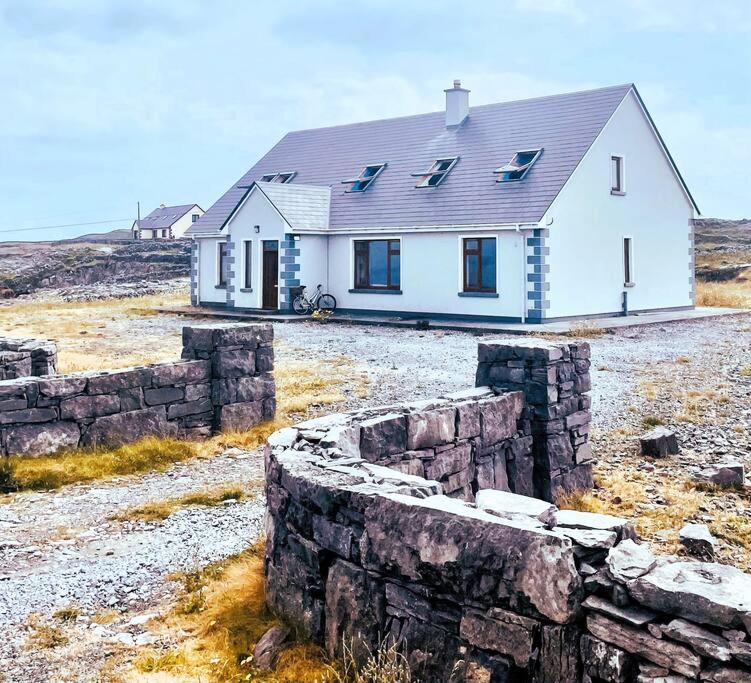 a white house in a field with a stone wall at Irish Isle Oasis: Spacious 5-Bedroom Retreat in Bungowla