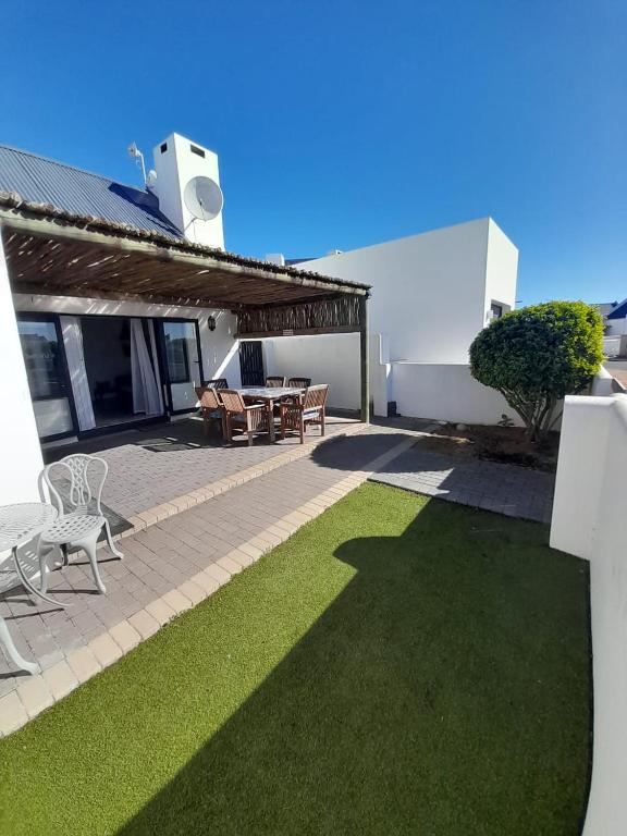 a patio with grass and a table and chairs at @ the reef Holiday Home in St. Helena Bay