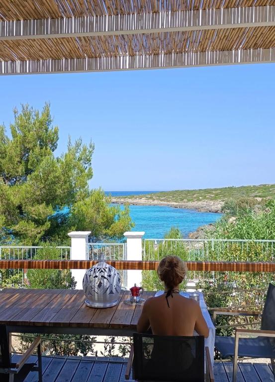 a woman sitting at a table on a deck looking out at the ocean at BAIA DELLE AGAVI in Taranto