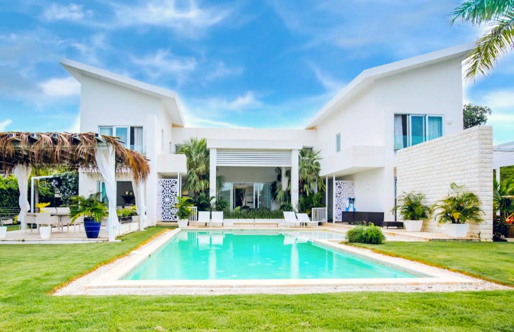 a white house with a swimming pool in front of it at Tranquil Lakefront 5-Bedroom Villa with Cook, Maid, Golf Cart, and Beach Access in Punta Cana in Punta Cana