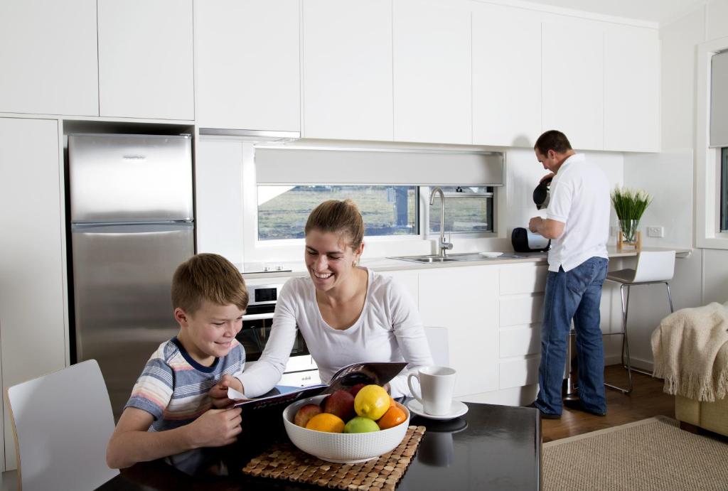 una mujer y un niño en una cocina con un tazón de fruta en Savannah Cabins, Taronga Western Plains Zoo, en Dubbo