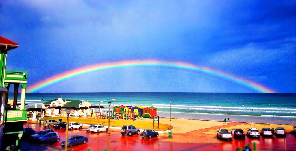 a rainbow over a beach with a parking lot at African Soul Surfer in Muizenberg