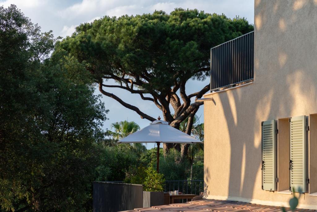 a white umbrella sitting next to a building with a tree at Hôtel L'Escalet in Ramatuelle