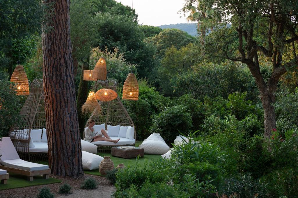 a woman sitting on a couch in a garden at Hôtel L'Escalet in Ramatuelle