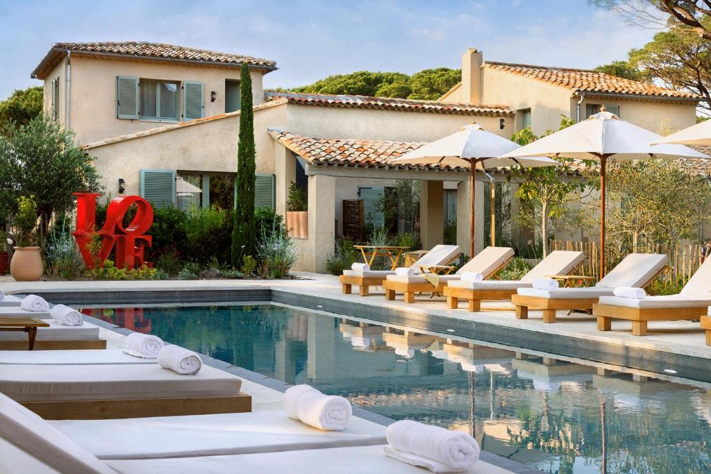 a pool with chairs and umbrellas next to a house at Hôtel L'Escalet in Ramatuelle