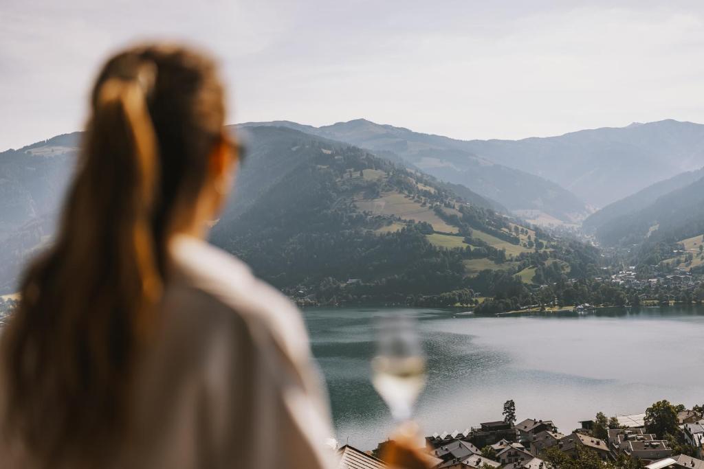 una mujer sosteniendo una copa de vino mirando un lago en Nikolaus by AvenidA Panoramic Wellness Suites, en Zell am See
