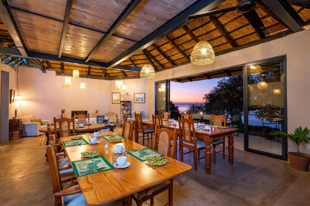 un ristorante con tavoli e sedie in legno e una grande finestra di Hornbill Lodge a Kariba