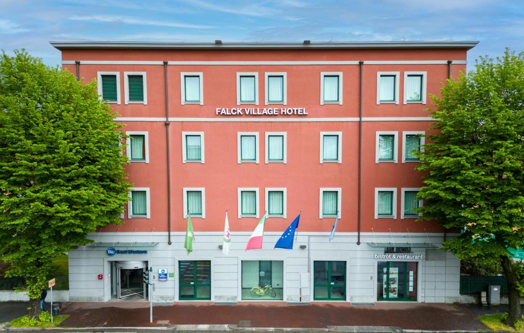 un bâtiment rouge avec des drapeaux devant lui dans l'établissement Best Western Falck Village Milano Sesto, à Sesto San Giovanni