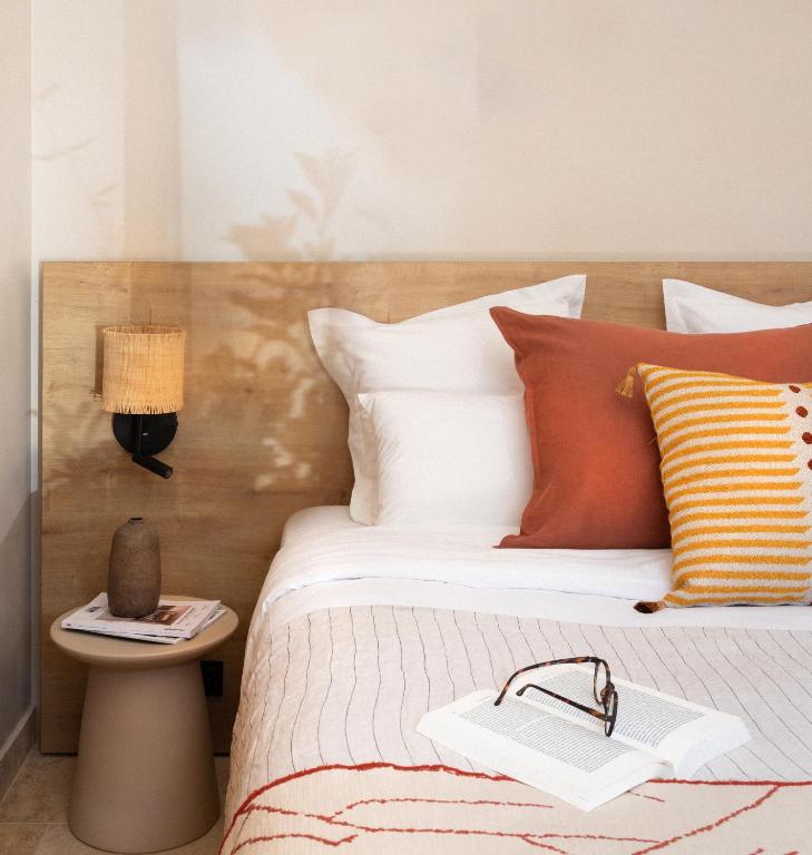 a bed with orange and white pillows and a book on it at Hôtel L'Escalet in Ramatuelle