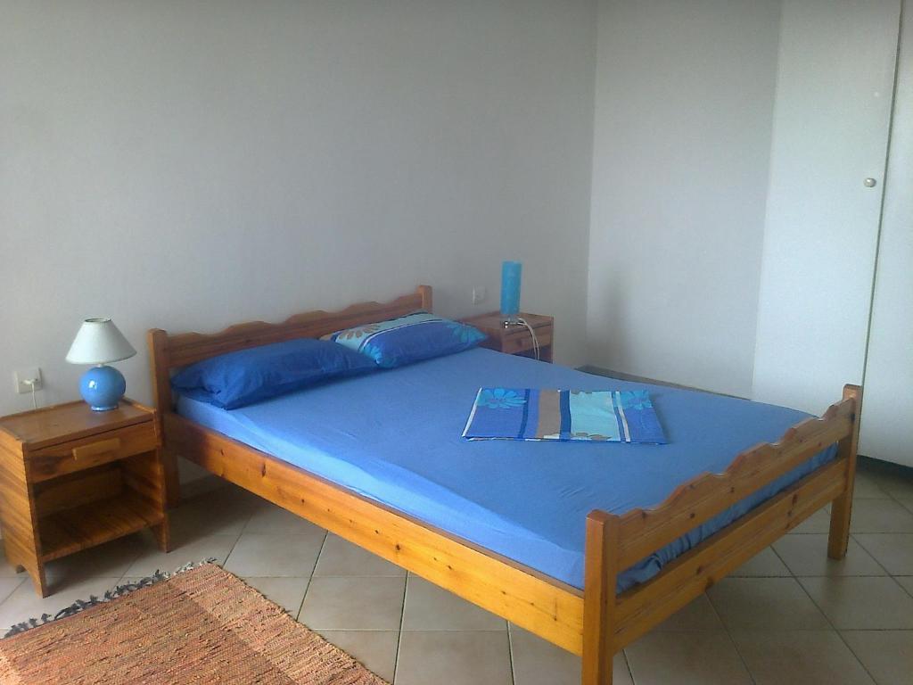 Schlafzimmer mit einem Holzbett mit blauer Bettwäsche und einem Tisch in der Unterkunft Appartement Epidaure vue sur mer 4 pers in Antikes Epidauros