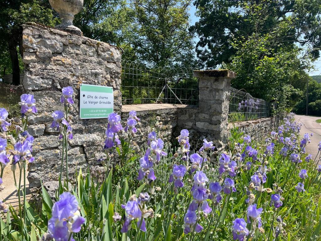 un jardín con flores púrpuras junto a una pared de piedra en Le Verger Grimaldin, en Grimault
