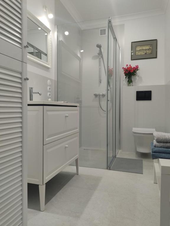a white bathroom with a shower and a sink at Apartament przy Wieży in Toruń