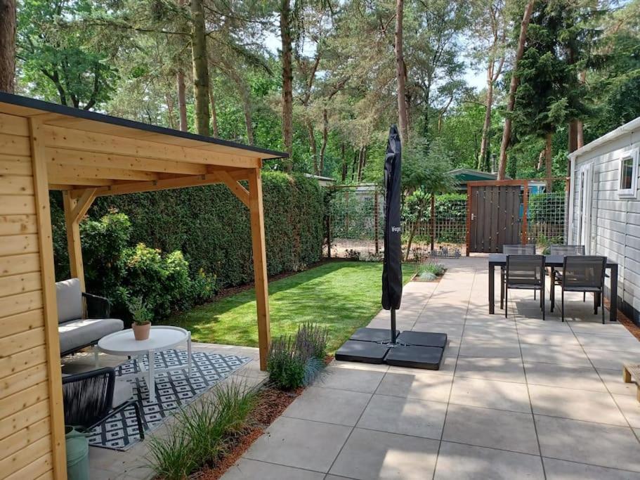 een patio met een paviljoen en een tafel en stoelen bij Boshuis met grote tuin I Vakantiepark met Zwembad in Hoenderloo
