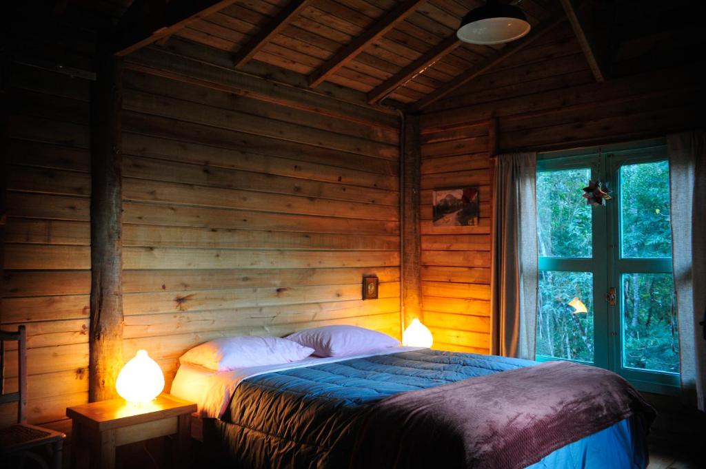 a bedroom with a bed in a wooden cabin with two lamps at Chalé Paiol - Sítio Lajinha in Alagoa