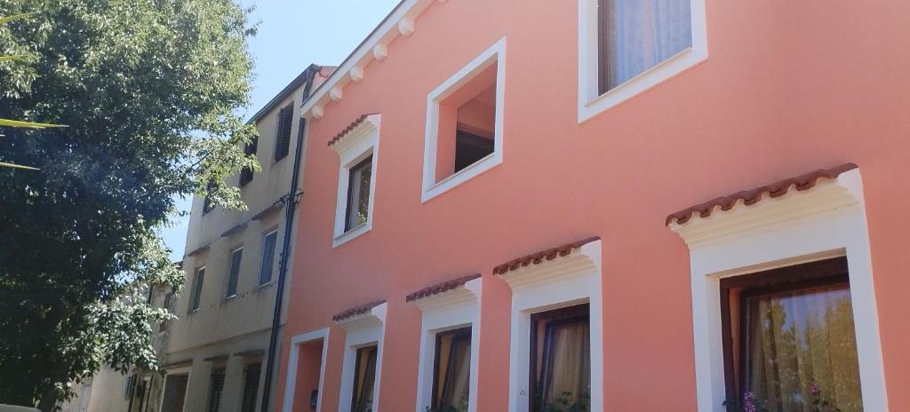 a pink building with white windows on a street at Apartments Velo in Veli Lošinj