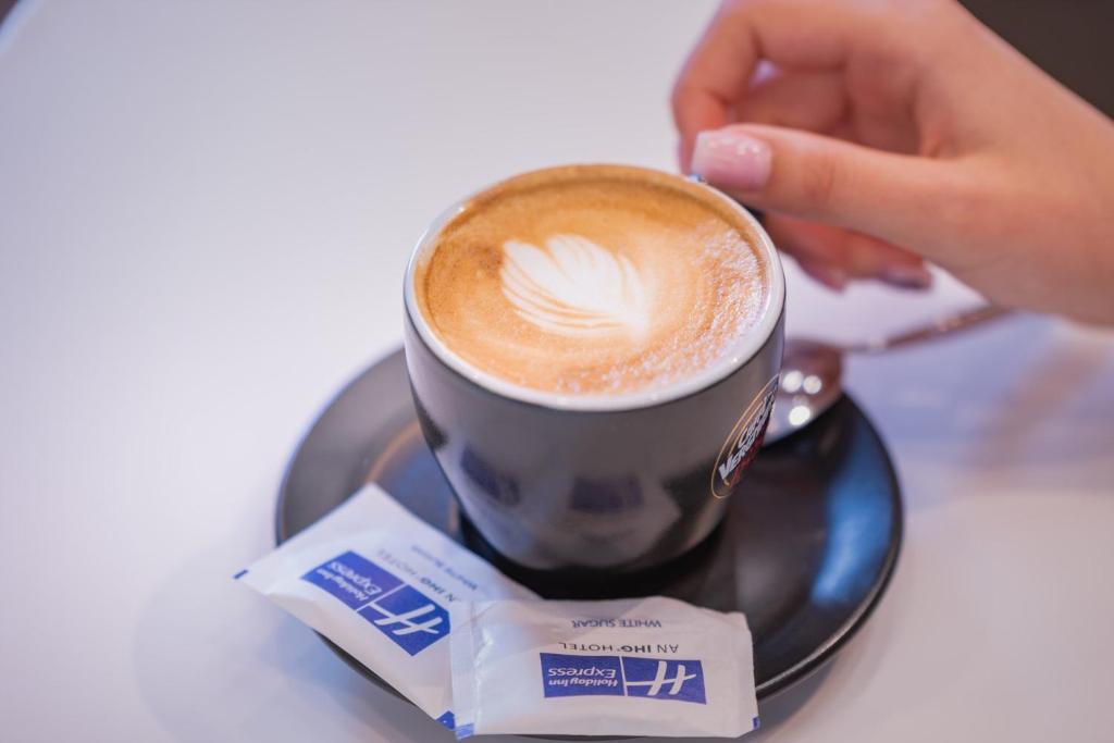 a person holding a cup of coffee on a plate at Holiday Inn Express - Yerevan, an IHG Hotel in Yerevan