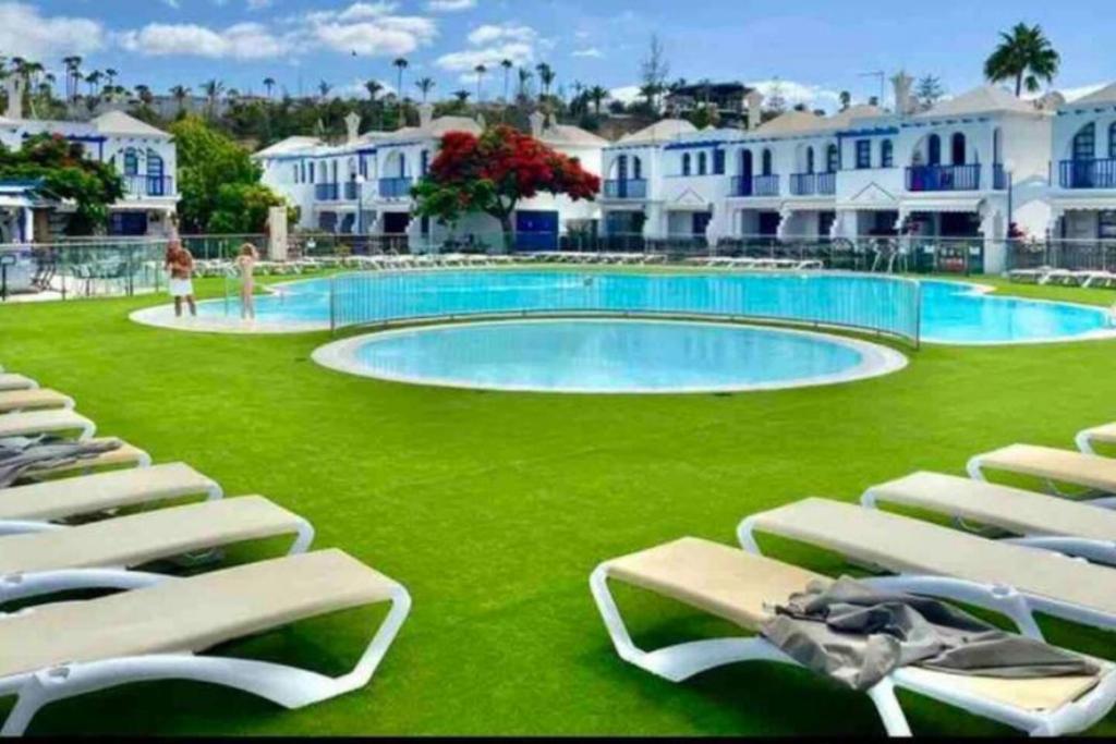 a large swimming pool with lounge chairs in front of a resort at Bungalow Maspalomas in Maspalomas