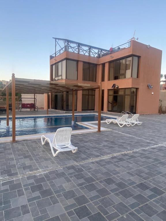 a building with a swimming pool and two white chairs at Jarash farm in Jerash