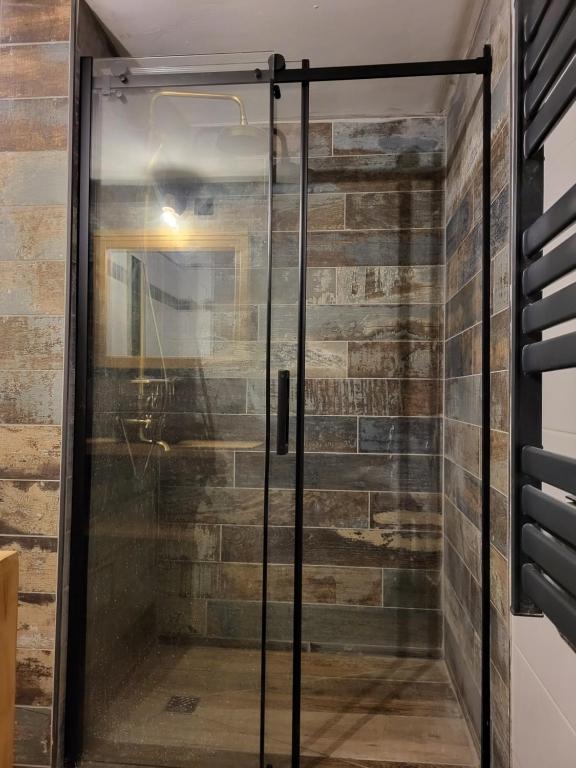 a glass shower door in a room with a brick wall at Appartement avec SPA et jardin in La Chapelle