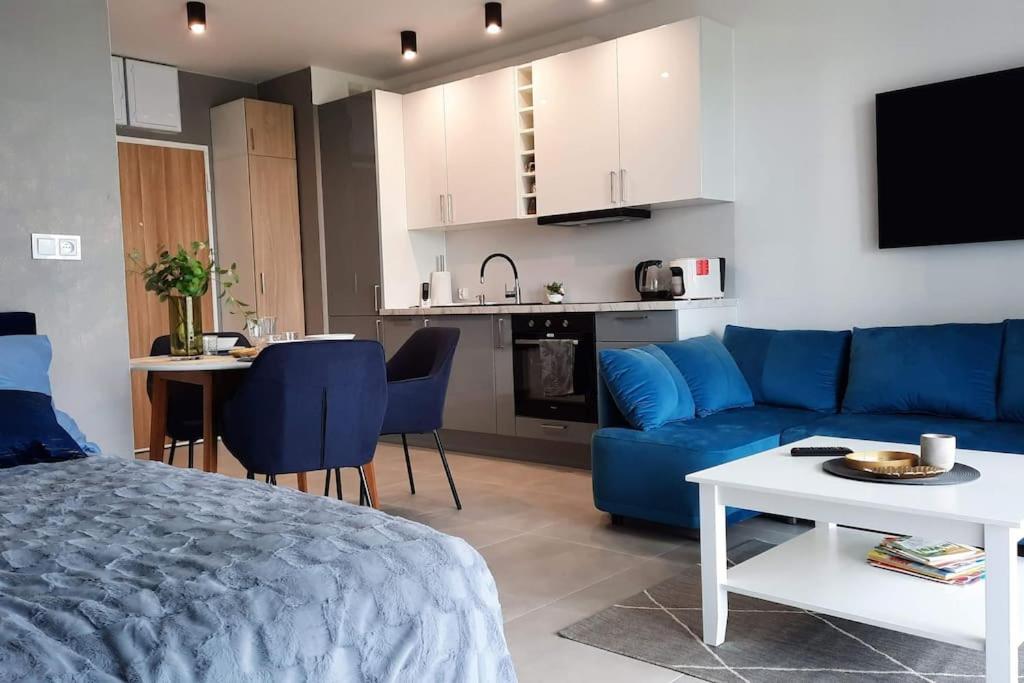 a living room with a blue couch and a kitchen at Apartament Błękitny Przy Morzu in Gąski