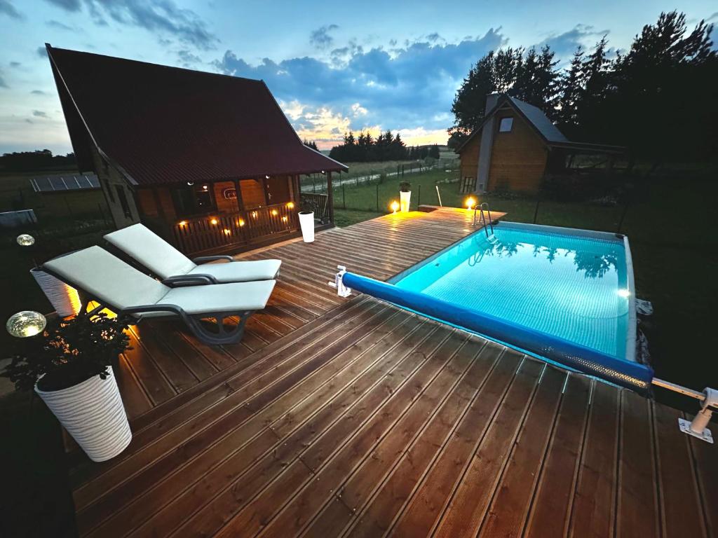 a wooden deck with a swimming pool and a chair and a bench at Domek letniskowy Jawor z basenem in Małdyty