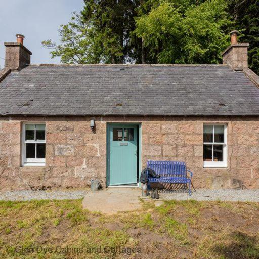 una casa de piedra con una puerta azul y un banco en The Bothy en Banchory