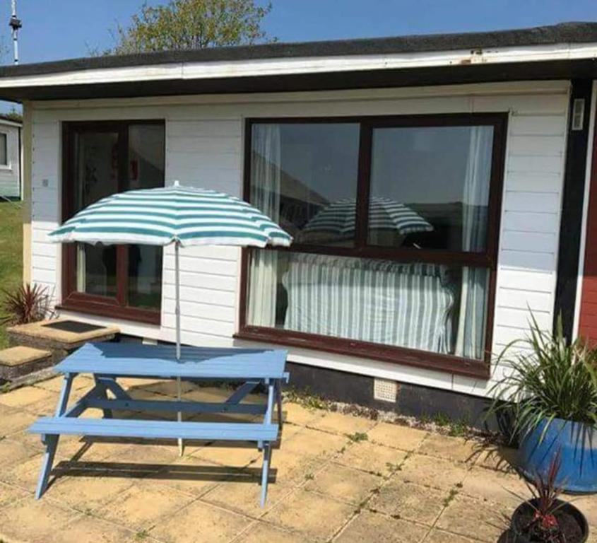 a blue picnic table with an umbrella in front of a house at 20 The Manor, Penstowe Holiday Park, Kilkhampton BUDE in Kilkhampton