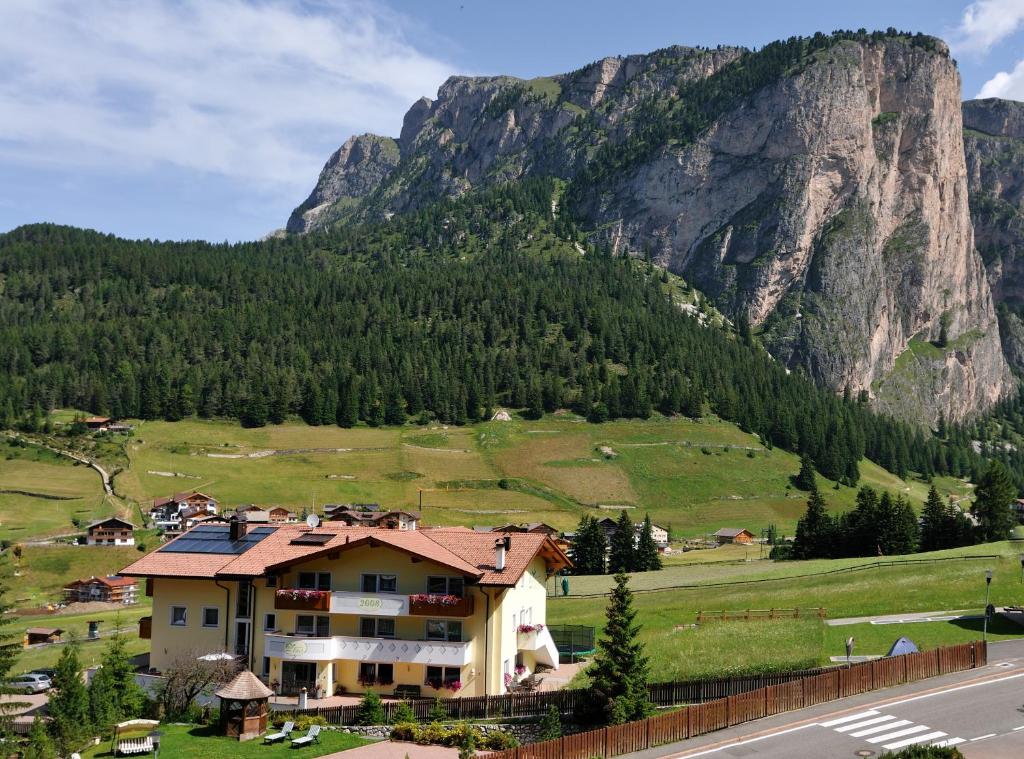 ein Haus auf einem Feld mit einem Berg im Hintergrund in der Unterkunft Garni Hotel Bel Vert in Wolkenstein in Gröden