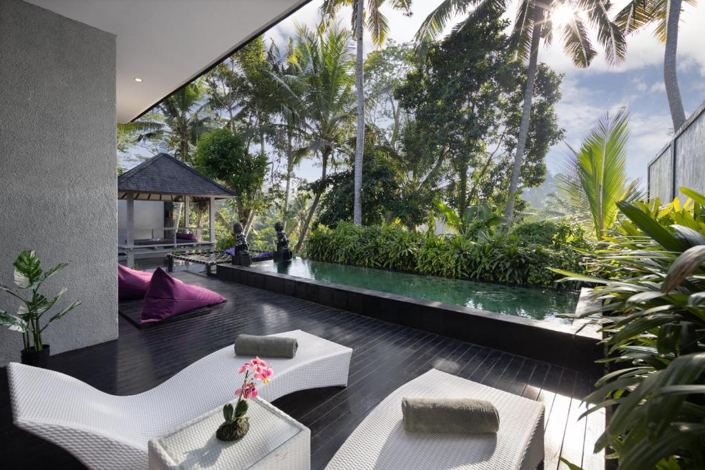 a room with a view of a garden with white furniture at Capung Asri Eco Luxury Resort with Private Pool Villas in Bedahulu