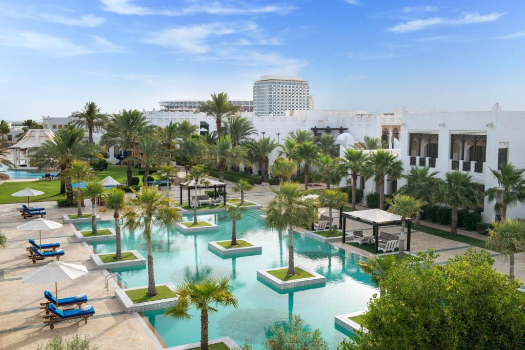 einen Luftblick auf einen Pool mit Palmen und Gebäuden in der Unterkunft Sharq Village & Spa, a Ritz-Carlton Hotel in Doha
