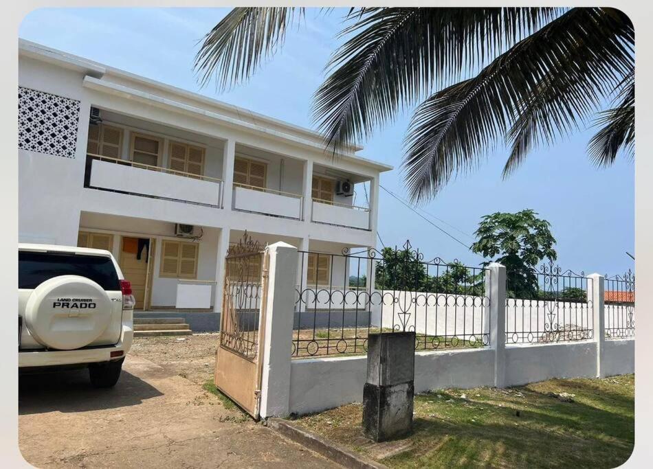 una casa blanca con una valla y un coche aparcado delante en Apartamento Vista Mar, en São Tomé